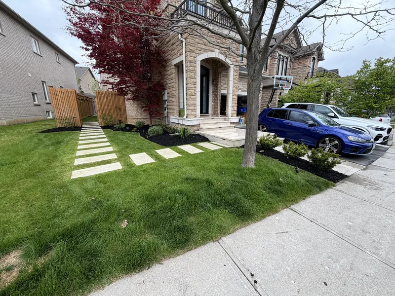 Rectangular stepping stones set into fresh lawn beside a dark mulch bed.