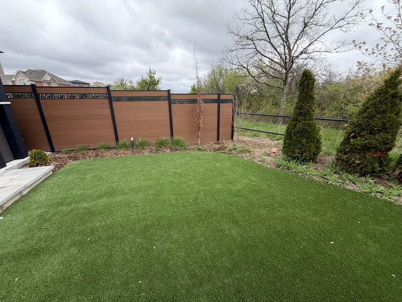 Artificial turf rear yard bordered by cedars against a dark composite fence.