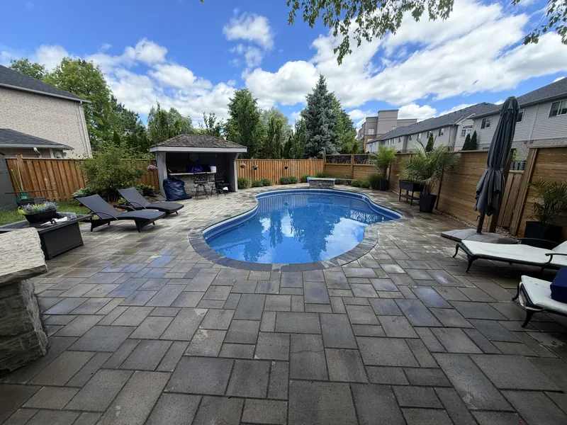 Interlock patio wrapping a curved pool with loungers and planted surrounds.