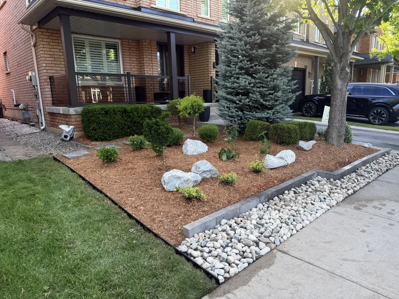 Front bed with boulders, a white river-rock border and fresh planting against the lawn.