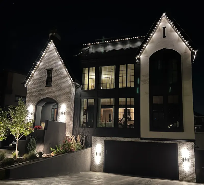 Warm white roofline lights traced along the gables and eaves of a house at night.